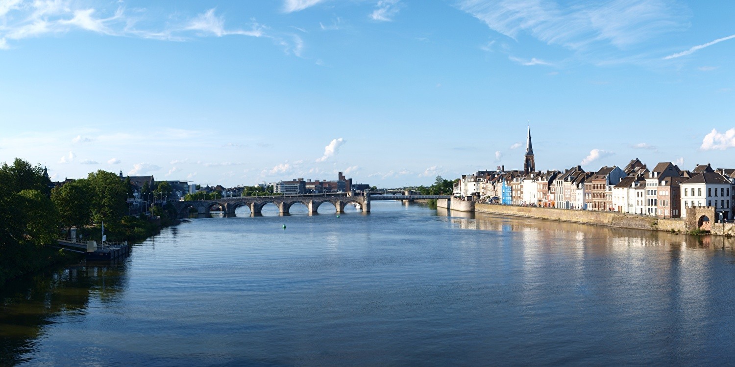 Panorama of Maastricht with a view of the Maas, the iconic Sint-Servaasbrug, and the historic facades along the quay under a blue sky.