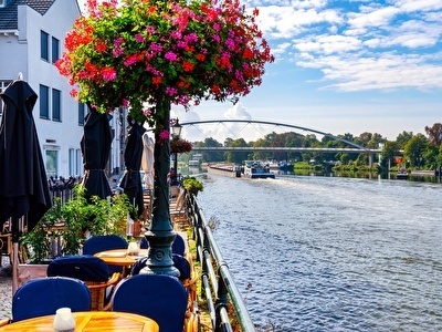 Terraces by the water with flowers, tables, and a view of a river.