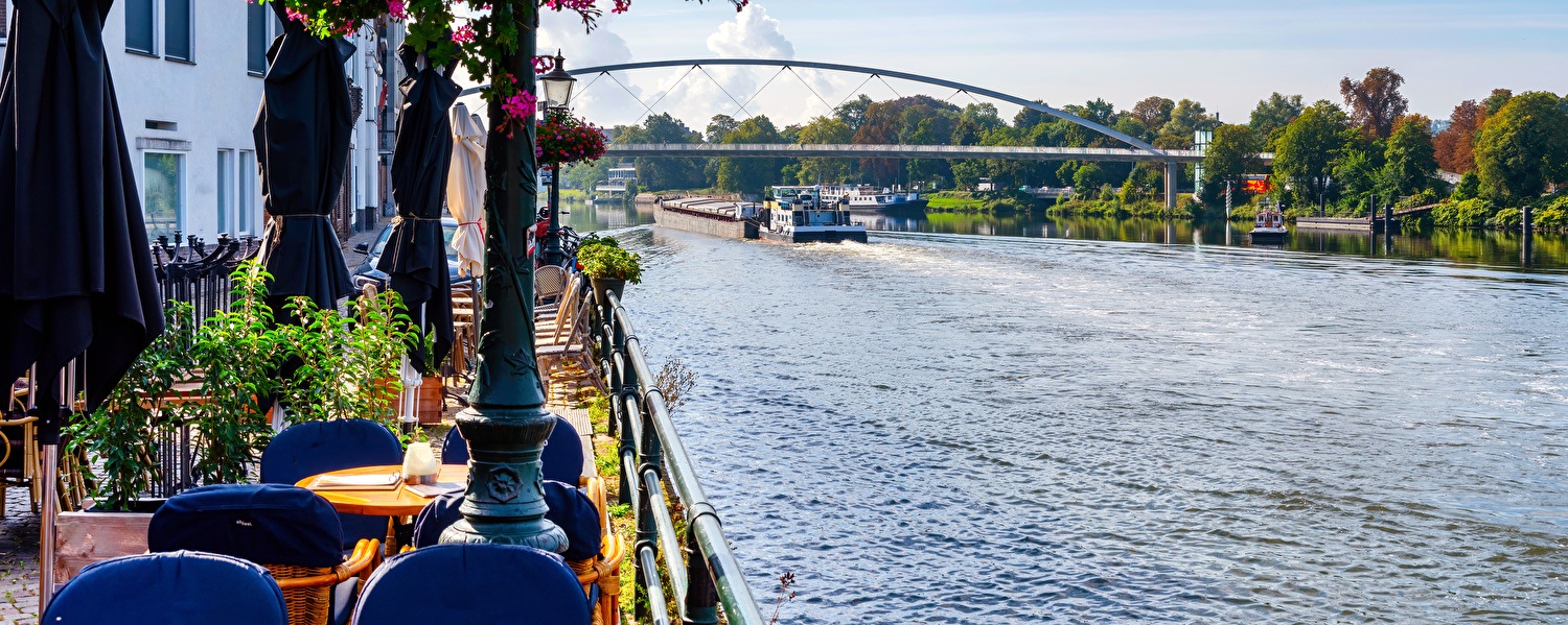 Terras aan het water met bloemen, tafels en uitzicht op een rivier.