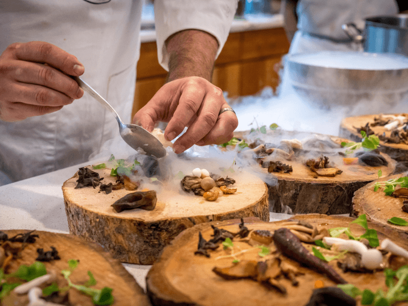 Chef is preparing a gastronomic dish with smoke and special ingredients on wooden serving boards.