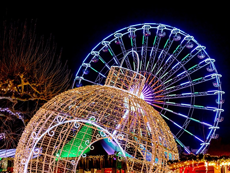 Verlichte kerstdecoraties en een grote reuzenrad ’s avonds tijdens een winterevenement, met kleurrijke lampjes en feestelijke sfeer