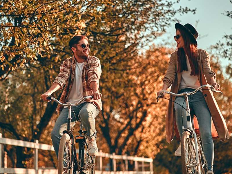 Mann und Frau fahren lachend nebeneinander auf einem sonnigen Herbsttag.