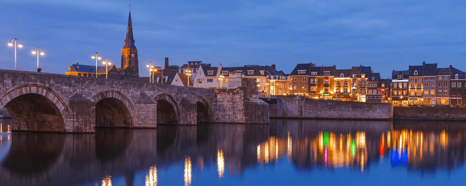 Abendblick auf die Sint-Servaasbrücke und die beleuchtete historische Altstadt von Maastricht, mit Reflexionen in der Maas.