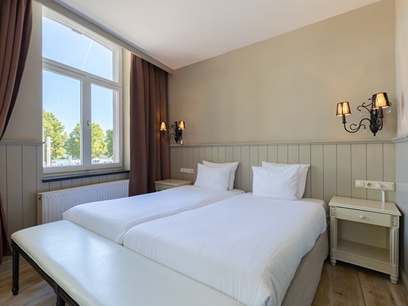 Deluxe room in Amrâth Hotel Bigarré with a twin bed with white sheets and white pillows and black classic chandeliers above the bed