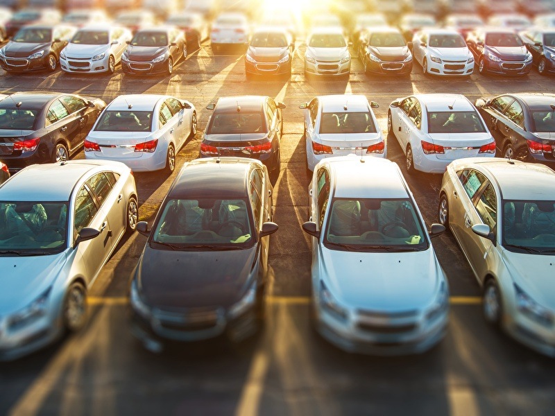 Ein Parkplatz mit mehreren Reihen geparkter Autos mit der untergehenden Sonne im Hintergrund